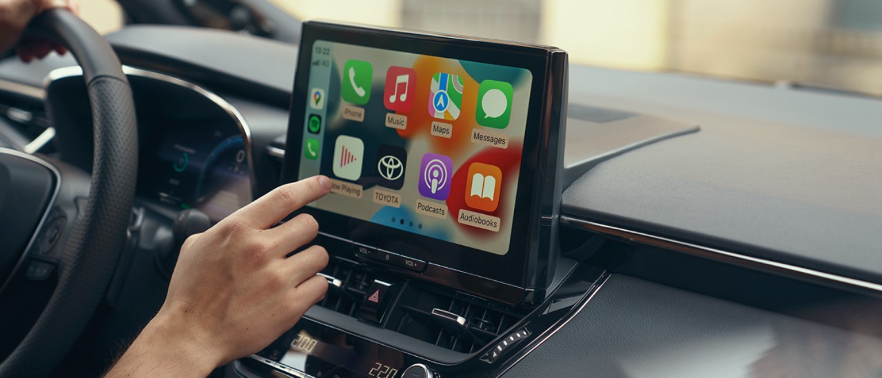 Een passagier in een Toyota bedient het multimedia touchscreen van de auto. Het display toont het startscherm van Apple CarPlay.
