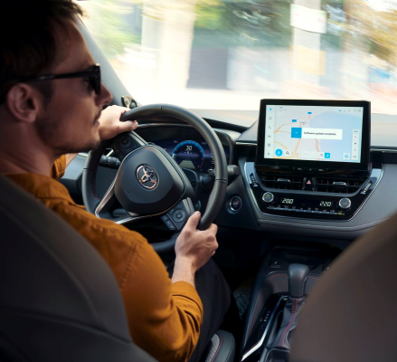 Een man in een oranje trui slaat rechtsaf in zijn Toyota. Het display van het multimediasysteem toont een software-update.