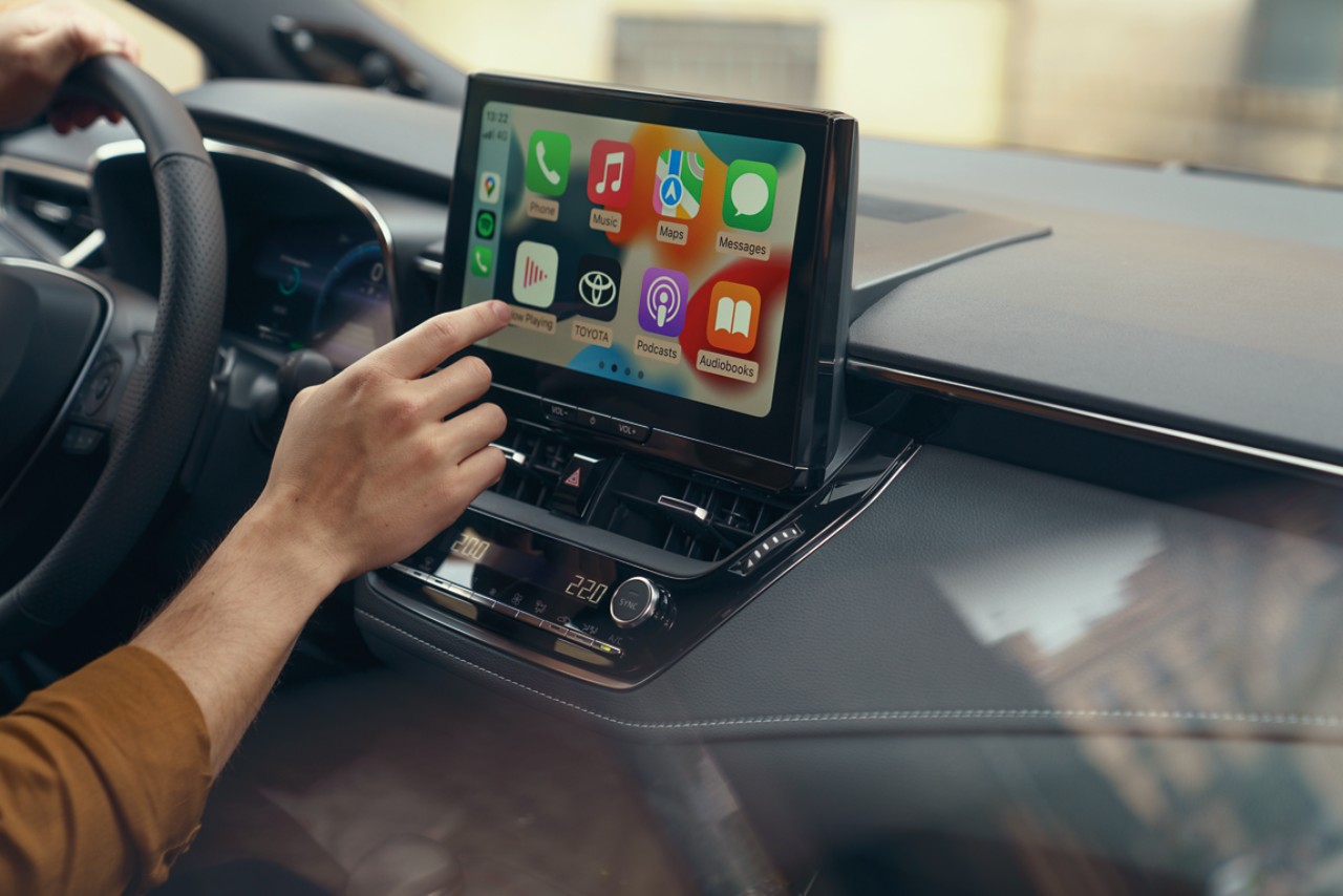 Een passagier in een Toyota bedient het multimedia touchscreen van de auto. Het display toont het startscherm van Apple CarPlay.